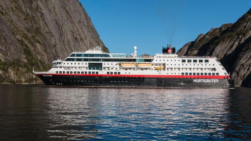 Passagierschiff Hurtigruten fährt durch norwegischen Fjord mit steilen Felswänden