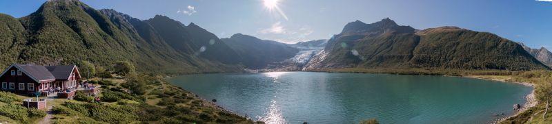 Berghütte am Ufer eines Bergsees mit Gletscher in der Ferne unter strahlendem Sonnenlicht