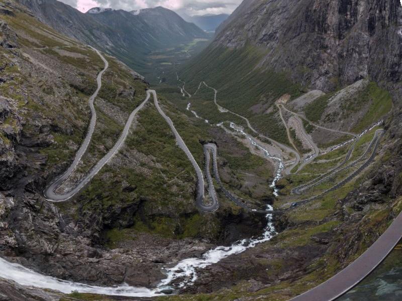 Serpentinenstraße windet sich durch eine felsige Berglandschaft mit Fluss im Tal darunter