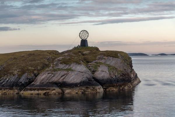 Kleiner felsiger Inselabschnitt mit einer großen Globus-Skulptur am Rand und ruhigem Wasser im Vordergrund