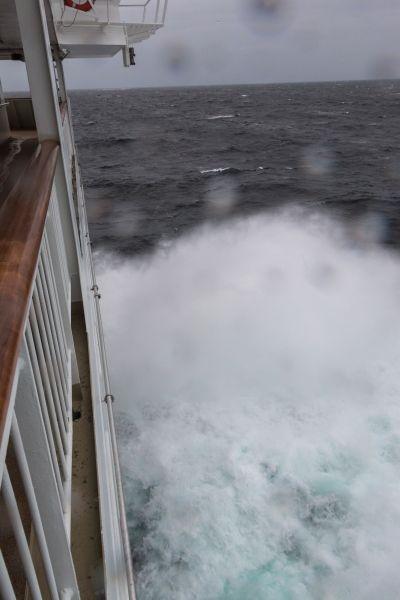Blick von der Reling eines Schiffes auf stürmisches Meer mit weißem Wellenschaum