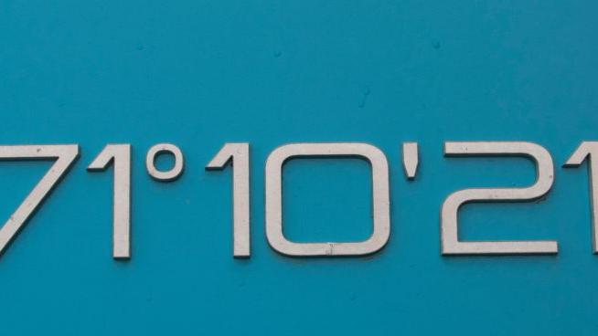 Weiße Zahlen und Symbole für Grad, Minuten und Sekunden an einer blauen Wand