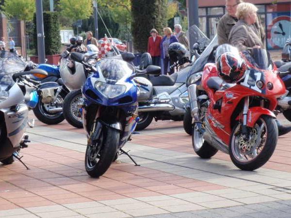 Drei Motorräder nebeneinander auf einem gepflasterten Platz mit Personen im Hintergrund