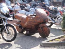 Mehrere Motorräder, darunter ein braunes hölzernes Motorrad, geparkt auf einem Gehweg