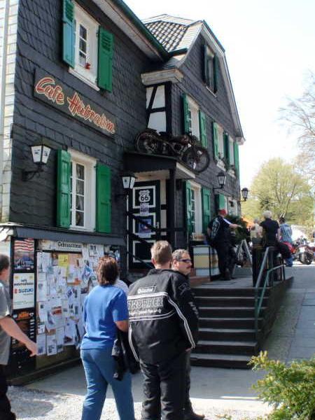 Traditionelles Fachwerkhaus mit grünen Fensterläden und Motorrädern vor dem Café und Menschen davor