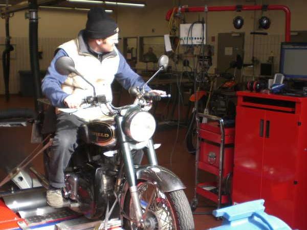 Person auf einem Motorrad in einer Werkstatt mit einem großen Ventilator davor