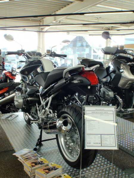 Moderne Motorräder stehen in einem hellen Ausstellungsraum auf Podesten aus Metall mit Preisschild und Informationsbroschüren.