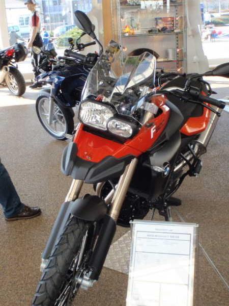 Rotes Motorrad auf einem Ausstellungsboden mit weiteren Motorrädern und einer Vitrine im Hintergrund