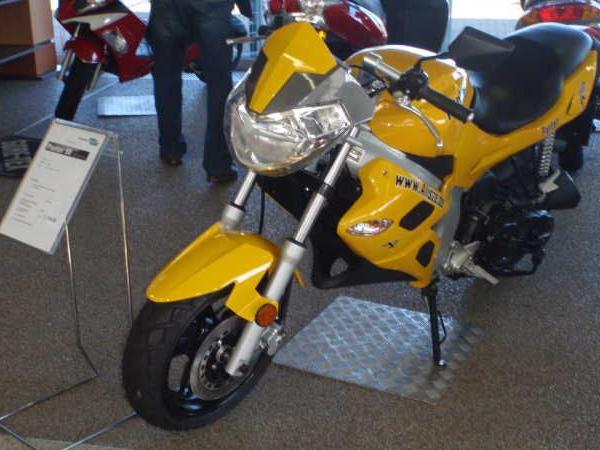 Gelbes Motorrad in einer Ausstellung auf Teppichboden mit Informationsschild