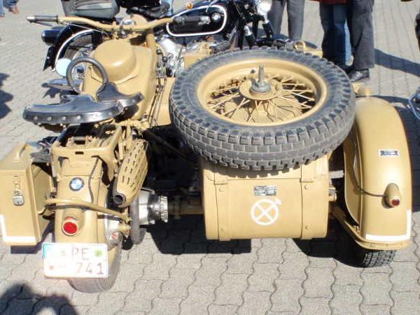 Beigefarbenes historisches Motorrad mit Seitenwagen und Ersatzreifen, umgeben von Menschen