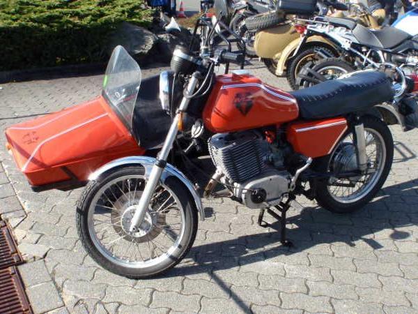 Rote Motorrad mit Beiwagen steht auf gepflastertem Parkplatz mit weiteren Motorrädern im Hintergrund