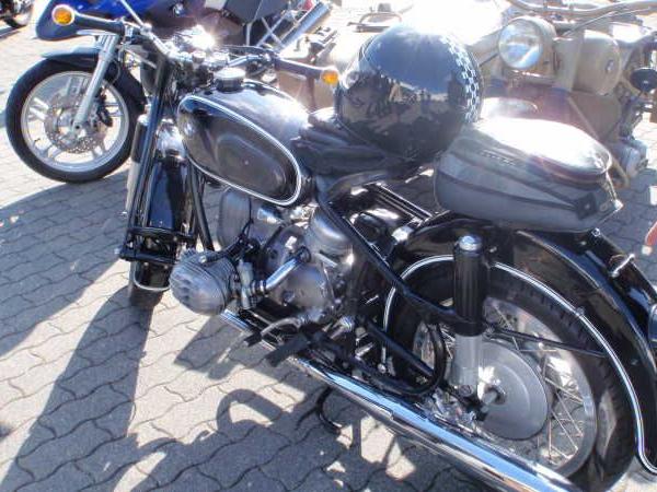 Schwarzes klassisches Motorrad mit Helm auf Sitz und Person zeigt auf Nummernschild