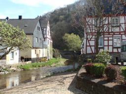 Fachwerkhäuser an einem kleinen Fluss in einem ruhigen Dorf mit Kopfsteinpflasterweg und Vegetation