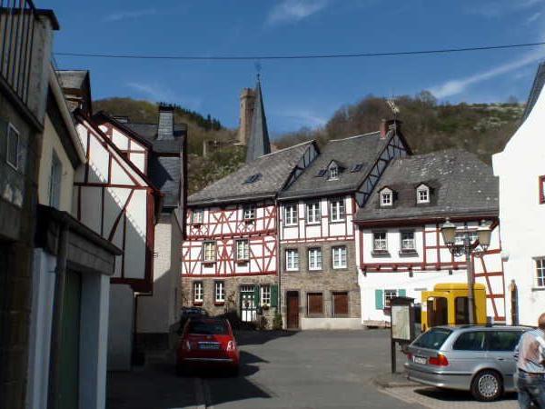 Straße mit Fachwerkhäusern, Autos und zwei Menschen in einer kleinen Ortschaft bei Sonnenschein