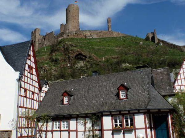 Fachwerkhäuser vor einer Burgruine auf einem Hügel unter blauem Himmel