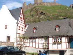 Panorama einer historischen Fachwerkhaussiedlung mit Burg auf einem Hügel im Hintergrund und geparkten Autos im Vordergrund