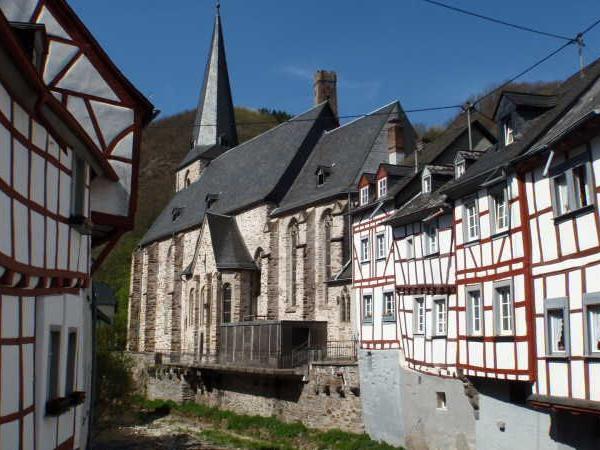 Fachwerkhäuser und eine Kirche mit steinernem Turm in einer engen Gasse unter blauem Himmel