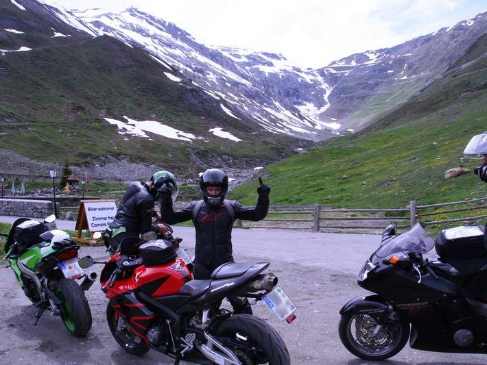 Drei Motorradfahrer mit ihren Motorrädern an einem Bergpass mit schneebedeckten Gipfeln