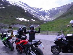 Drei Motorradfahrer mit ihren Motorrädern an einem Bergpass mit schneebedeckten Gipfeln