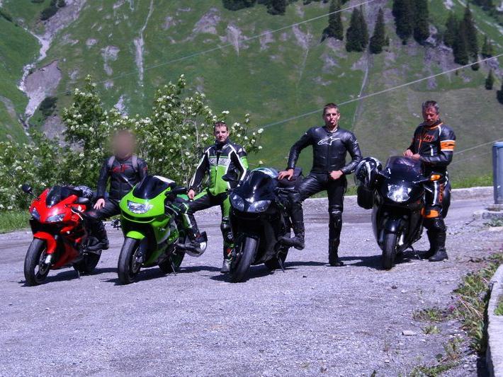 Vier Motorradfahrer in Lederkleidung neben ihren Motorrädern in alpiner Landschaft