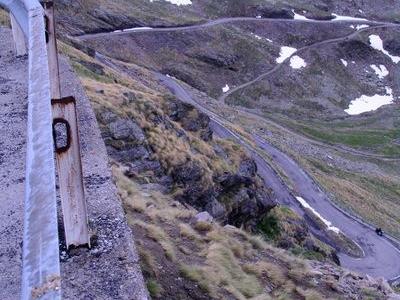 Bergstraße mit Haarnadelkurven und Geländer bei schneebedeckten Gipfeln
