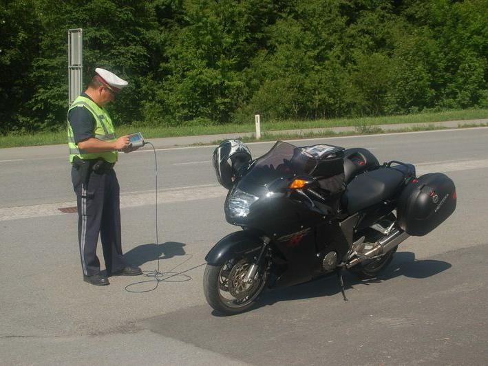 Polizist steht neben einem schwarzen Motorrad und bedient ein Messgerät auf einer Straße.