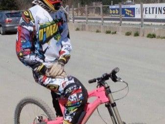 Fahrradfahrer mit buntem Schutzanzug und Helm sitzt auf pinkfarbenem Mountainbike auf Asphaltfläche