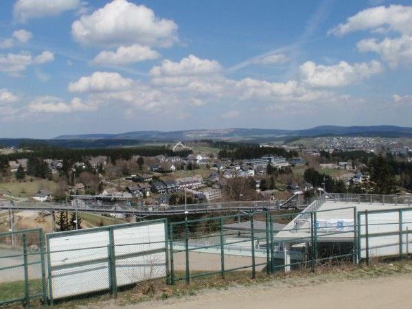 Blick auf eine Stadt mit Wohnhäusern, Waldgebieten und Bergen unter blauem Himmel mit Wolken