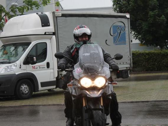 Motorradfahrer mit Helm und Schutzkleidung fährt vor einem weißen Lieferwagen auf nasser Straße