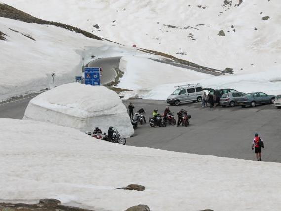 Parkplatz in einer verschneiten Berglandschaft mit Motorrädern, Autos und einer großen Schneehöhle