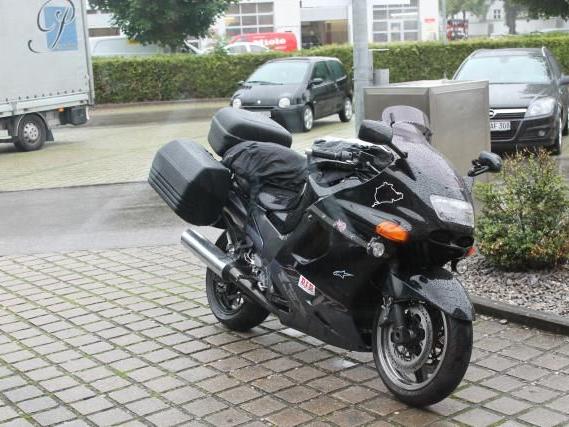 Schwarzes Sportmotorrad mit Koffern auf einem gepflasterten Parkplatz neben parkenden Autos