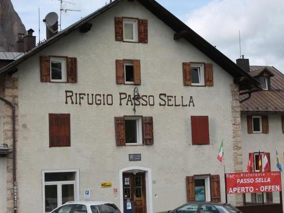 Außenansicht eines bergigen Gasthauses mit Schriftzug Rifugio Passo Sella und zwei geparkten Autos davor