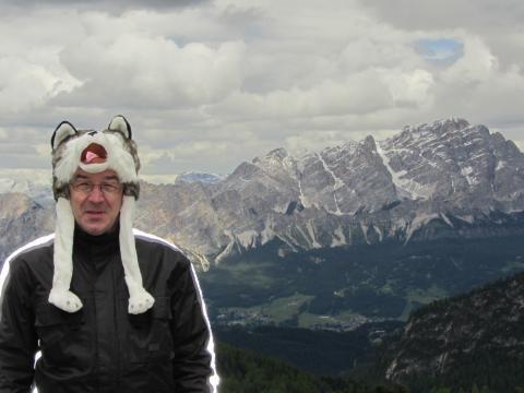 Mann mit lustiger Tiermütze vor Berglandschaft mit Wolkenhimmel