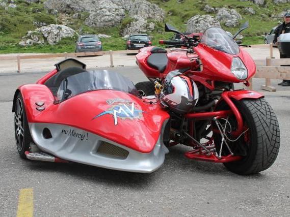 Rotes Motorrad mit speziellem Beiwagen auf asphaltierter Fläche vor Felsen und Gras
