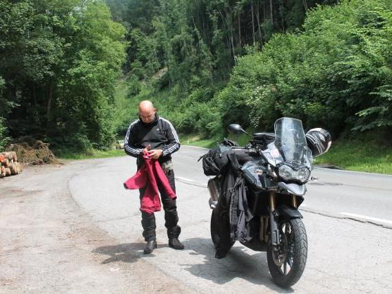 Mann mit Motorrad an Waldrand auf ruhiger Landstraße