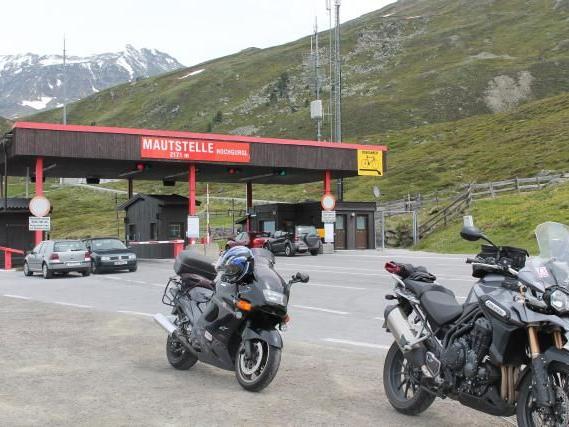 Mautstelle auf einer Bergstraße mit zwei geparkten Motorrädern und bergiger Landschaft im Hintergrund