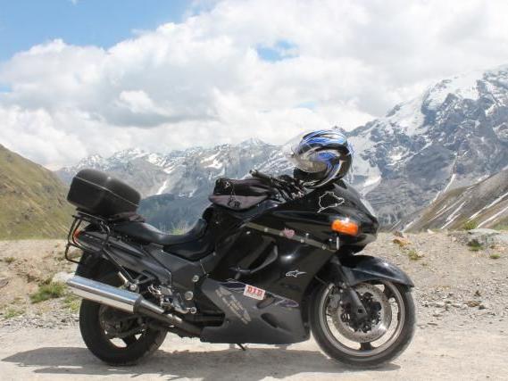 Schwarzes Motorrad mit Helm auf einer Gebirgsstraße vor schneebedeckten Bergen