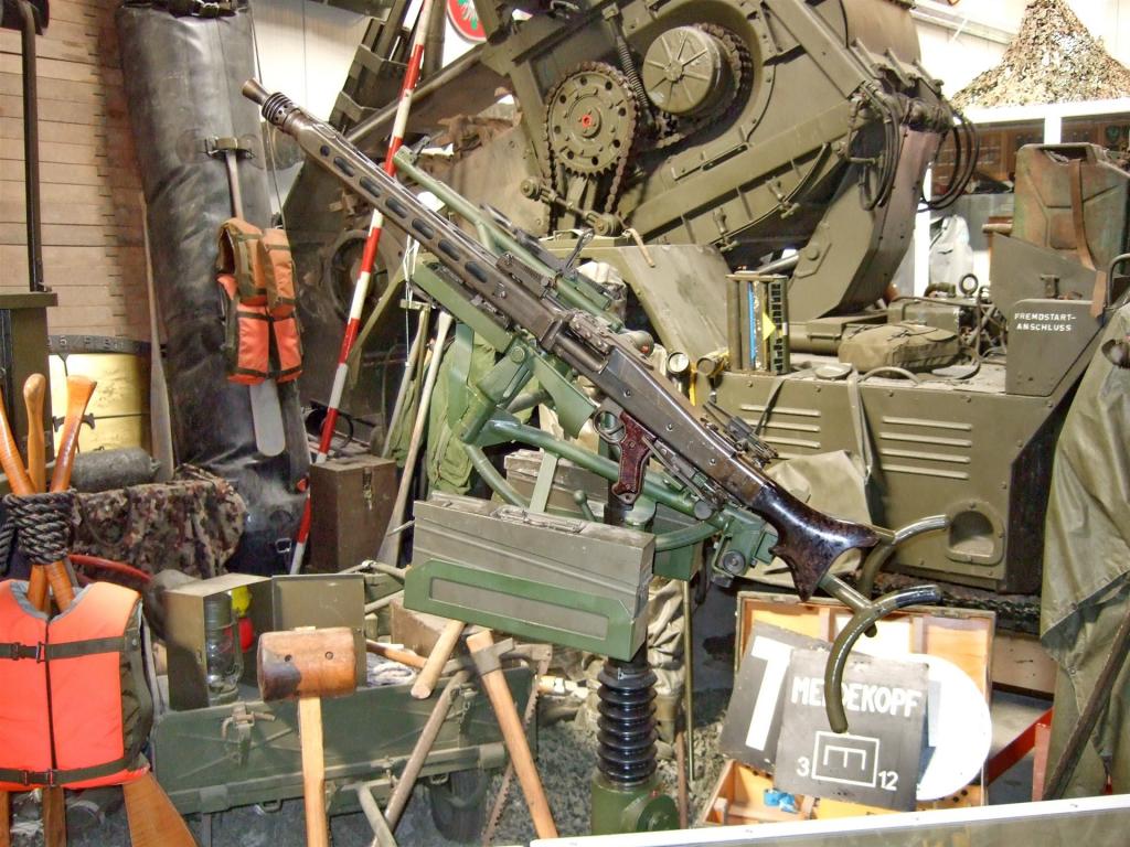 Maschinengewehr auf einem Stativ in einem militärischen Ausstellungsraum mit Ausrüstung und Fahrzeugen im Hintergrund