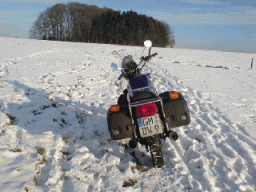 Motorrad mit Gepäcktaschen steht schräg im schneebedeckten Feld unter blauem Himmel