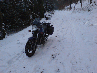 Motorrad steht auf einem schneebedeckten Waldweg in winterlicher Landschaft